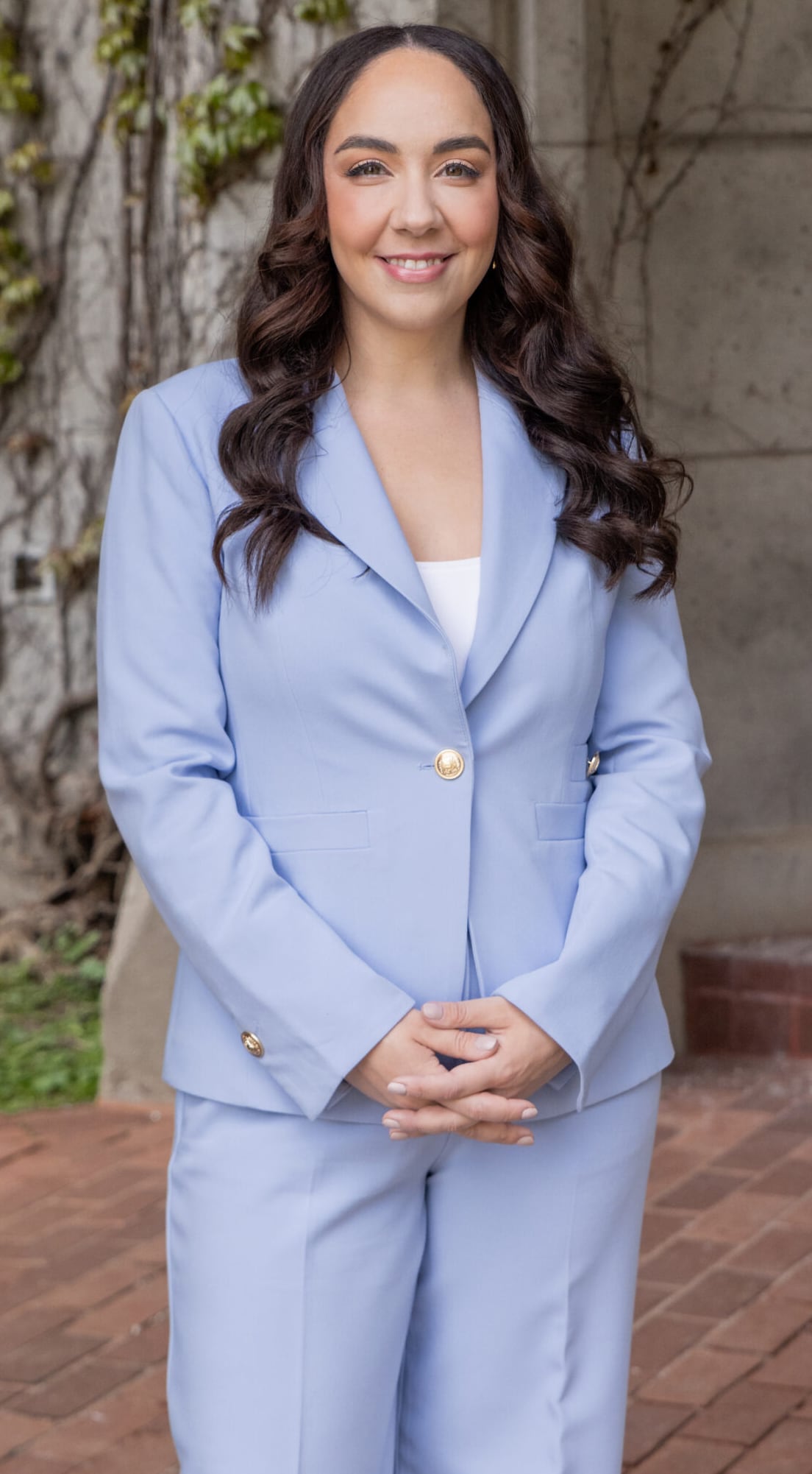 Woman in blue suit stands with hands folded