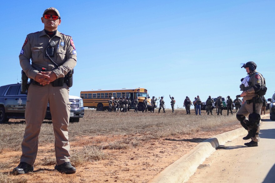 Texas DPS troopers in riot gear line up near a school bus outside the Dilley immigration detention center during a protest Wednesday, Jan. 28, 2026.