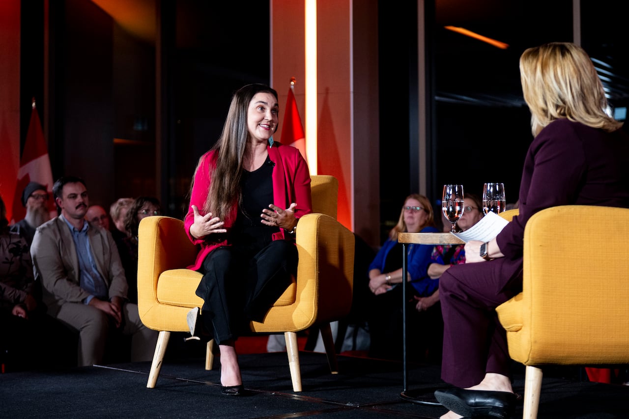 Two woman sit on a stage as the crowd looks on