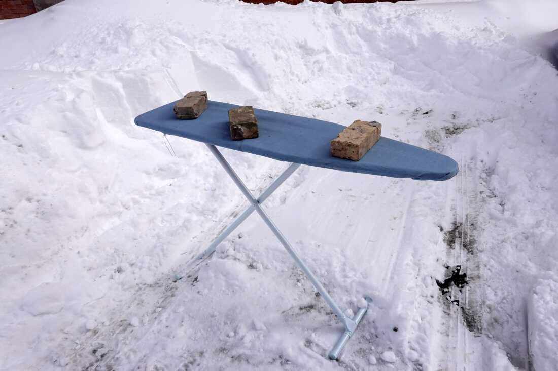 A resident uses an ironing board to save a parking spot on the street after shoveling out a car in a system that is referred to as "Dibs" in in Chicago on Feb. 16, 2021 .