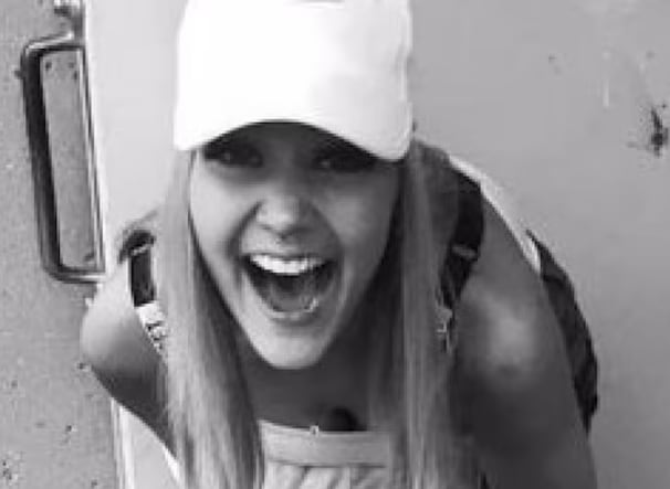 A black and white image of a woman with long hair wearing a white ball cap.