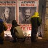 People wearing winter coats attend a candlelight vigil where Alex Pretti was killed in Minneapolis. Large posters of Alex Pretti and Renee Macklin Good are on a wall, and candles are on the ground in front of the posters.