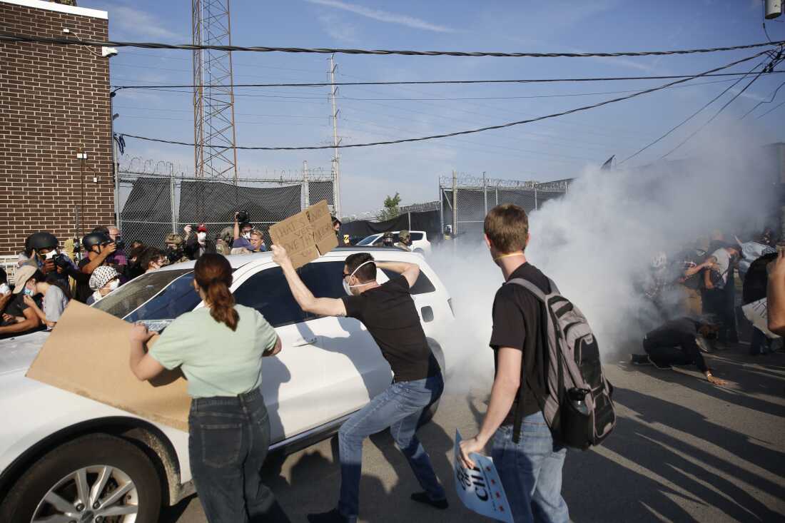Pro-immigration demonstrators try to stop a car leaving an ICE processing center during a protest in Broadview, Ill., on Sept. 19, 2025. A white cloud appears behind the car.