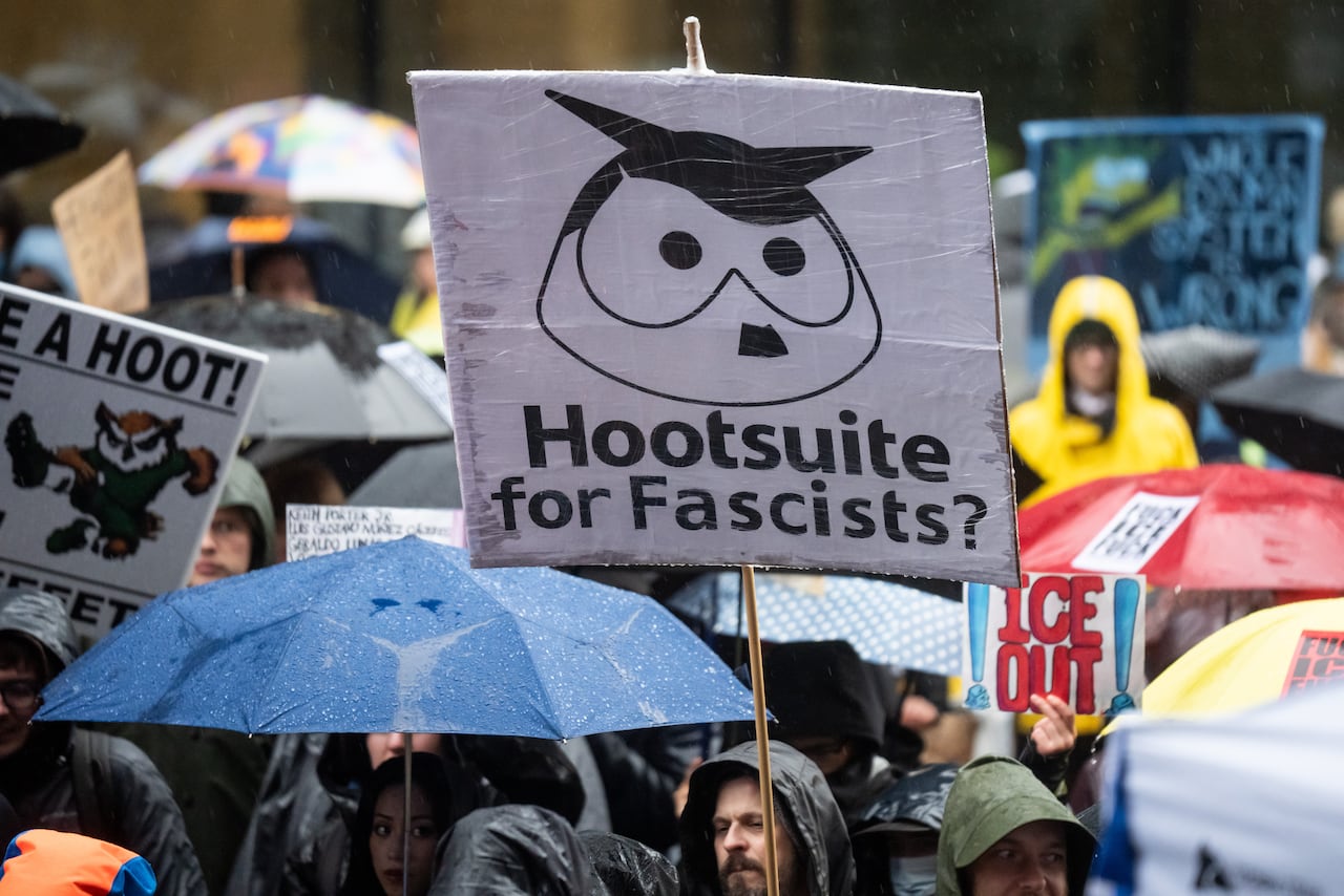 A sign at a protest, mocked up to be like an owl with a Hitler moustache reads 'Hootsuite for Fascists?'