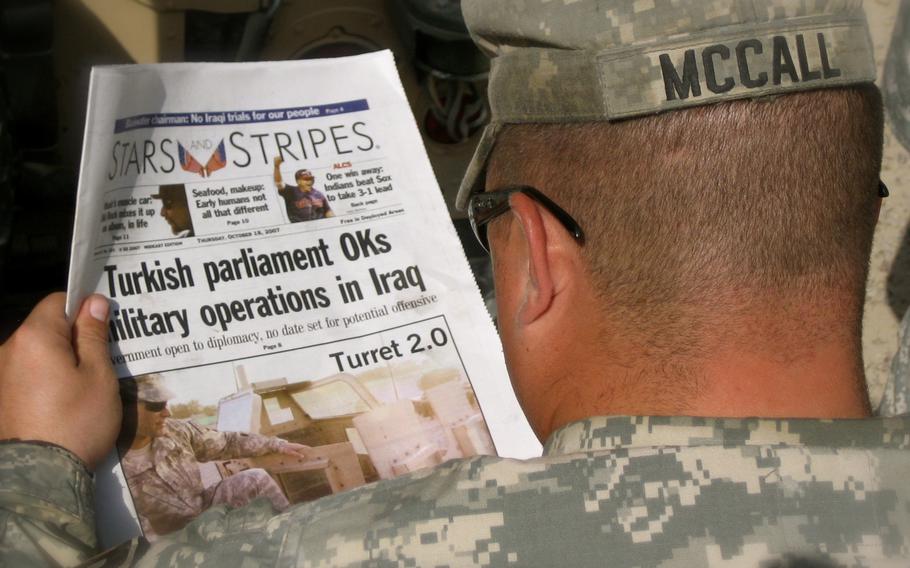The Stars and Stripes newspaper is seen past the shoulders of a soldier.