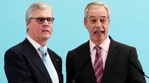 PA Media Malcolm Offord, who has grey hair and glasses, next to a smiling Nigel Farage, who has thinning grey hair. Both are wearing dark suits, and standing in front of a pale blue background. 