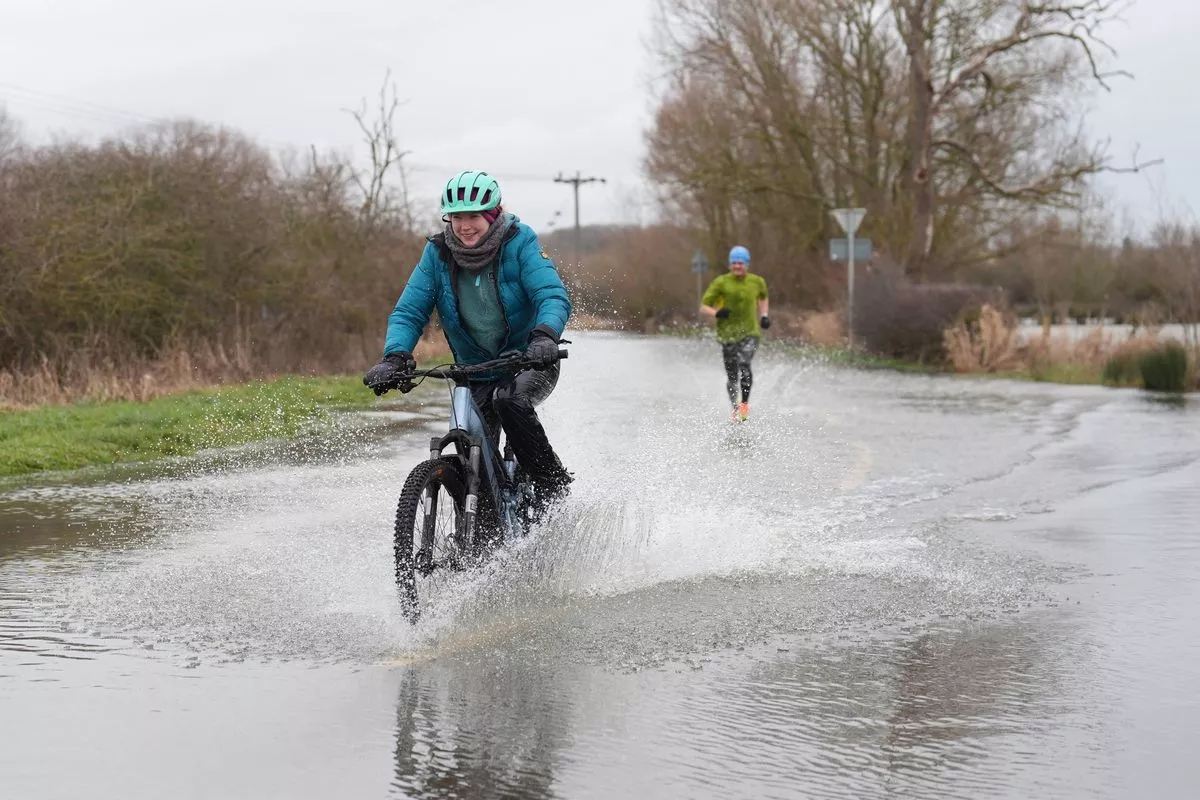 People cycle and run along a flooded road in Mountsorrel, Leicestershire