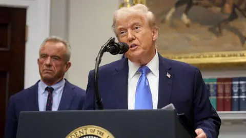 Getty Images US President Donald Trump talks into a microphone in the White House, with Robert F. Kennedy Jr, US Health Secretary on his left, on 22 September 2025, wearing a navy blue suit and sky-blue tie