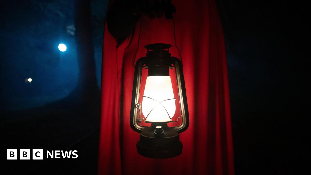 A red-cloaked figure carrying a lamp on The Traitors