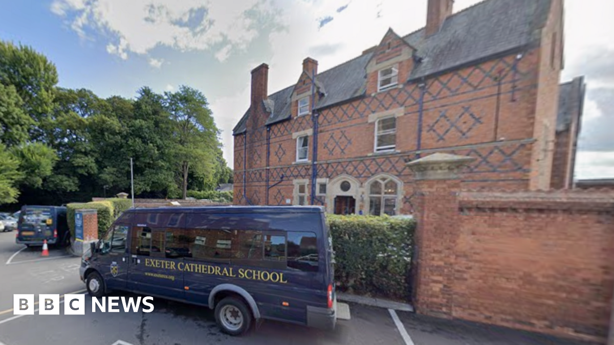 An street view of outside of Exeter Cathedral School. There is a blue bus outside of the building with the words 'Exeter Cathedral School'. The building is brown with blue details.