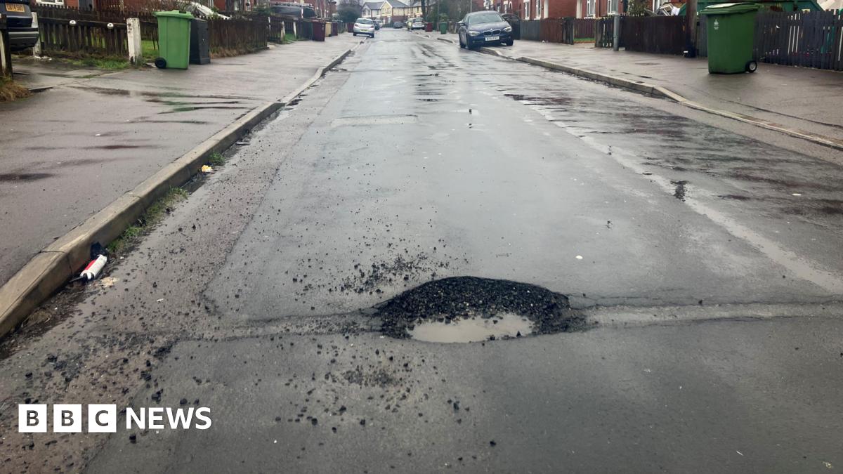 Prime Minister Mark Carney, wearing a black suit jacket, and a white button-up shirt leans his chin on his hands. He has short grey and black hair and is looking away from the camera.