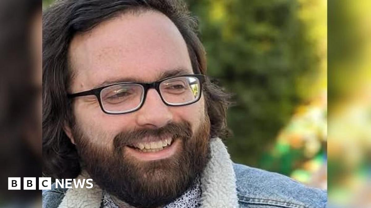 A bearded man wearing glasses. He is wearing a fleeced denim jacket.
