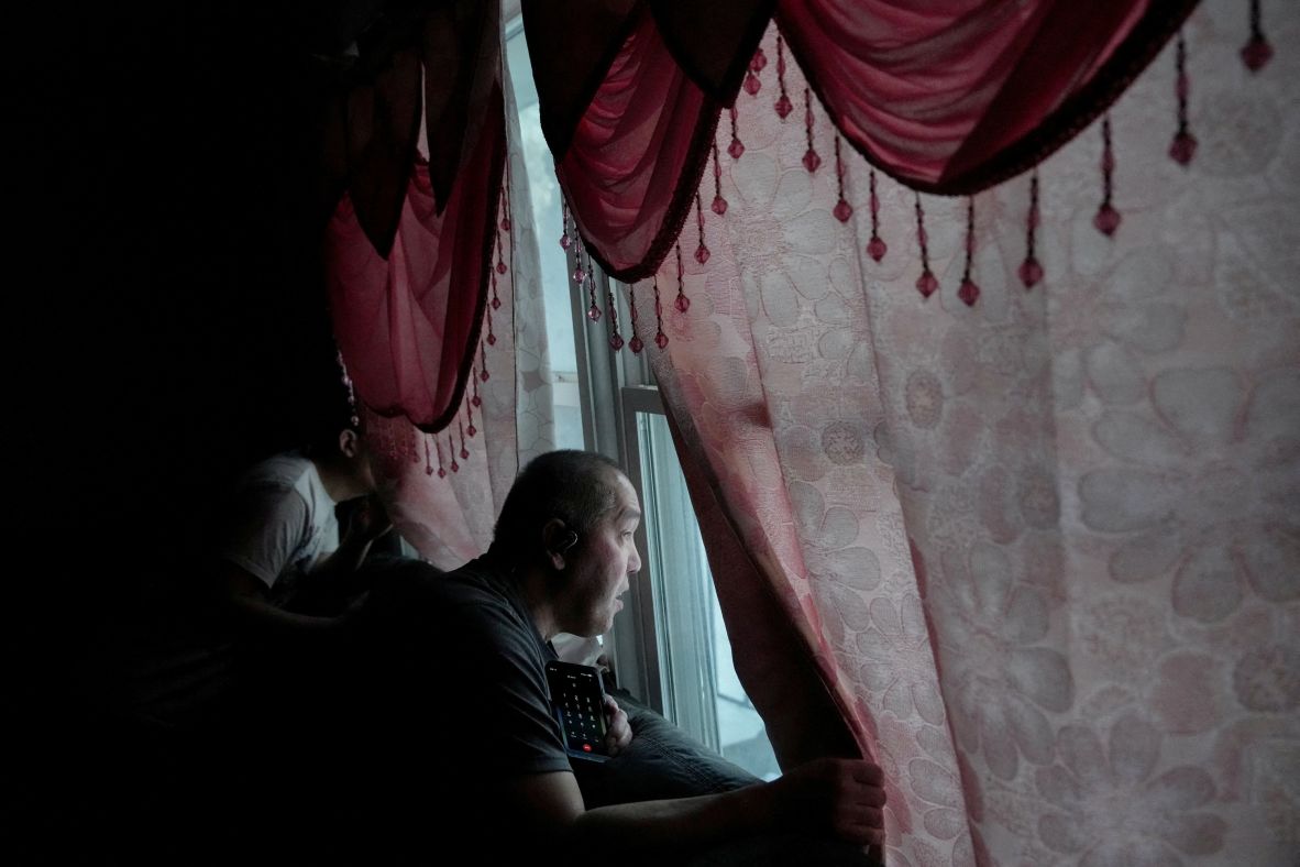 Thao looks out the window with his son Chris as several vehicles with ICE agents idle in the street outside of their home a day after he was taken from his home.