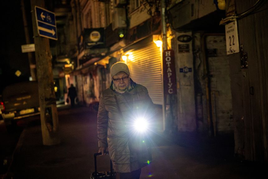 A woman uses a flashlight on her phone to walk along a dark street during a blackout in Kyiv on December 10, 2025.