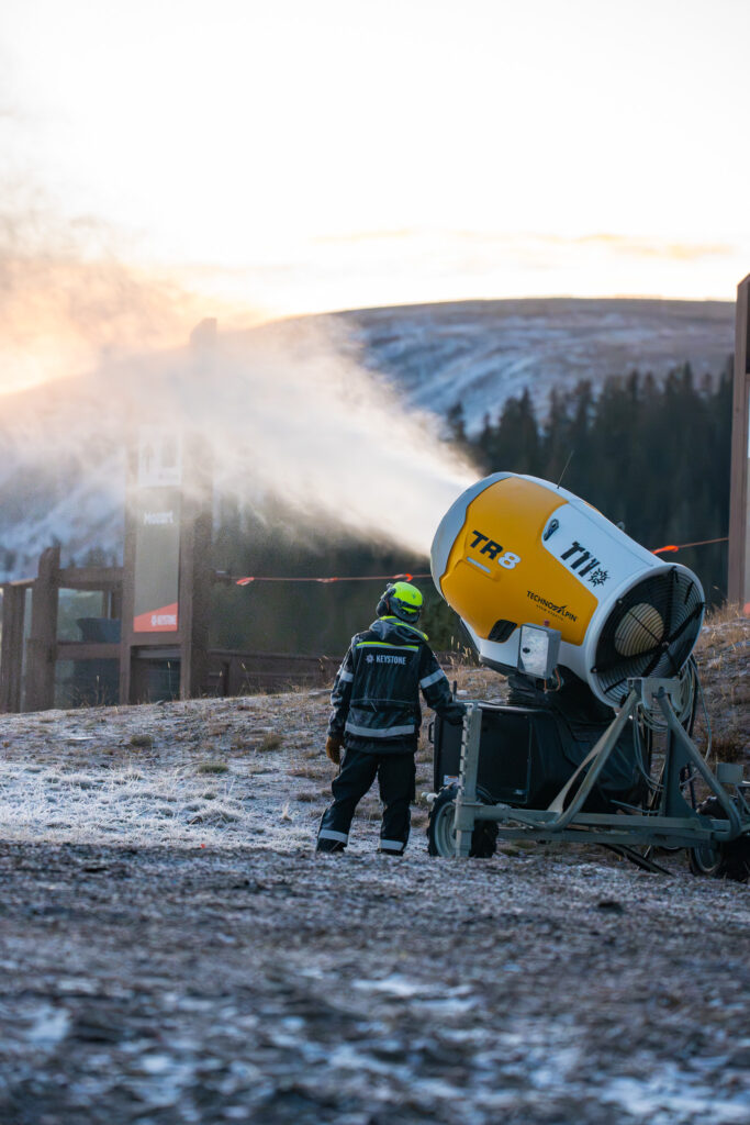 A person stands beside a snowmaking machine spraying snow