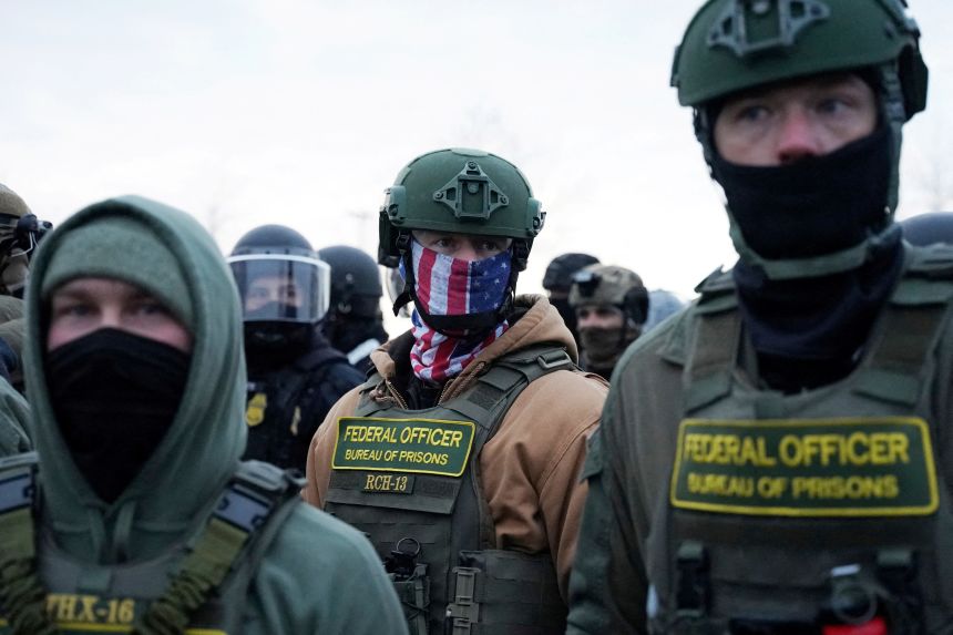 Federal agents stand in front of the Bishop Henry Whipple Federal Building during a protest in Minneapolis Saturday.