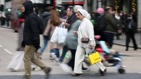 Reuters People walk with shopping bags on Oxford Street during Boxing Day sales, in London.