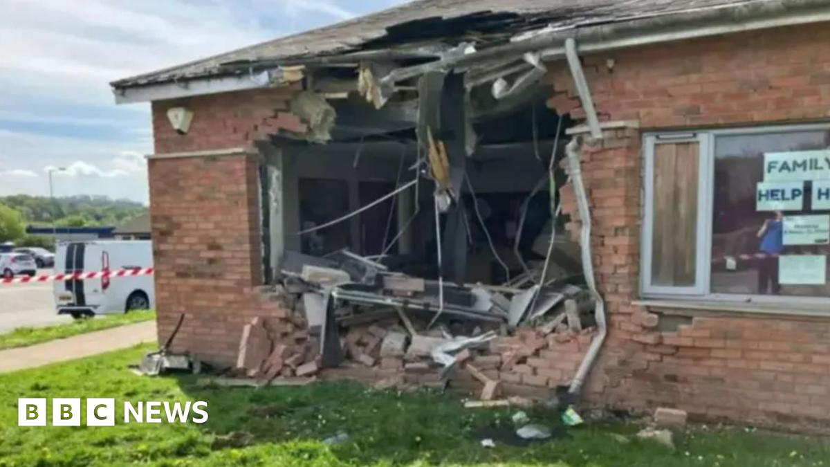 A one storey brick building with a large hole smashed in the side of it and grass surrounding the building