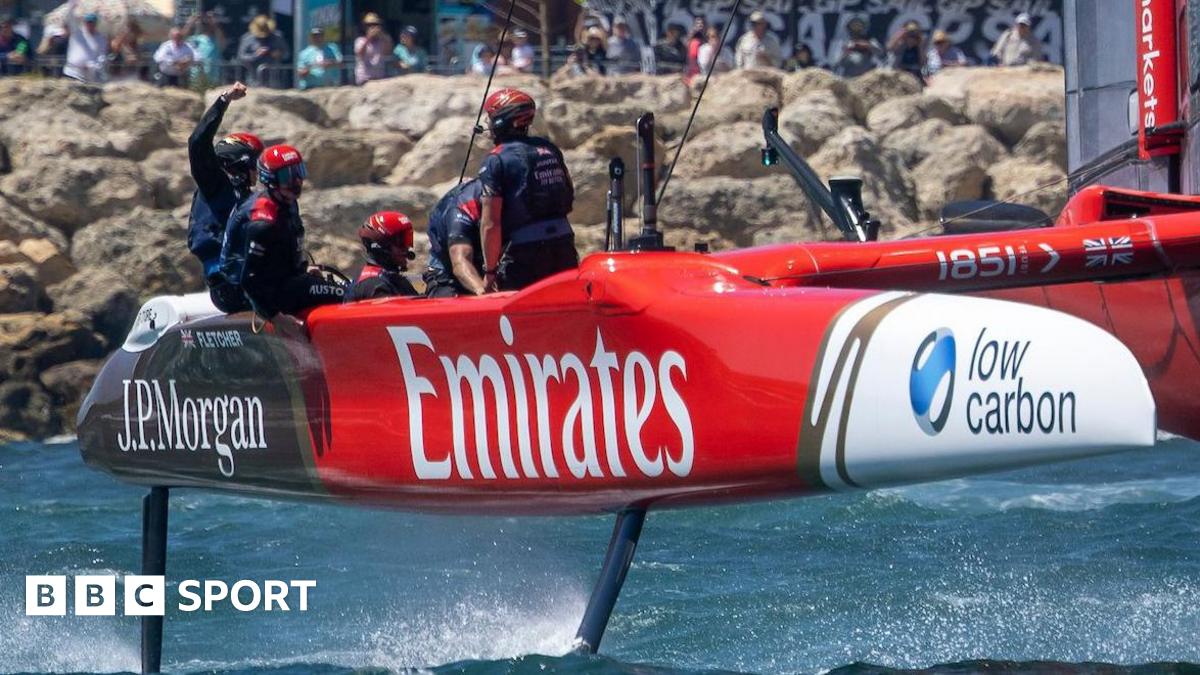 Great Britain's SailGP team celebrate on their catamaran after crossing the finish line. The craft has large sponsor logos for Emirates and JP Morgan.