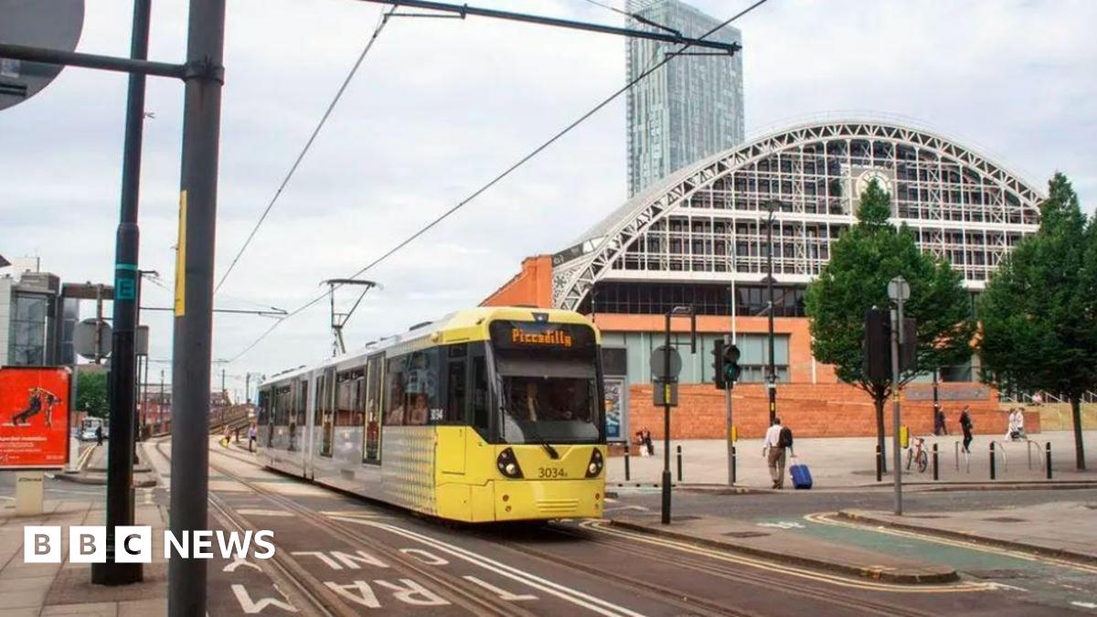 A yellow tram with Piccadilly on the front passes Manchester Exhibition Centre heading towards St Peter's Square tram stop.