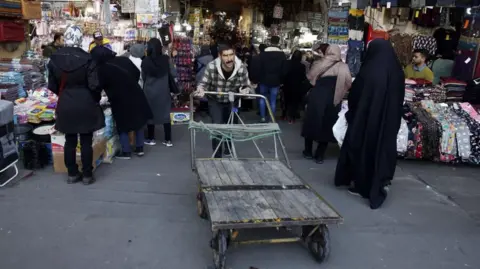 EPA A man pushes a wooden trolley, as people walk through the Grand Bazaar in Tehran (file photo) 
