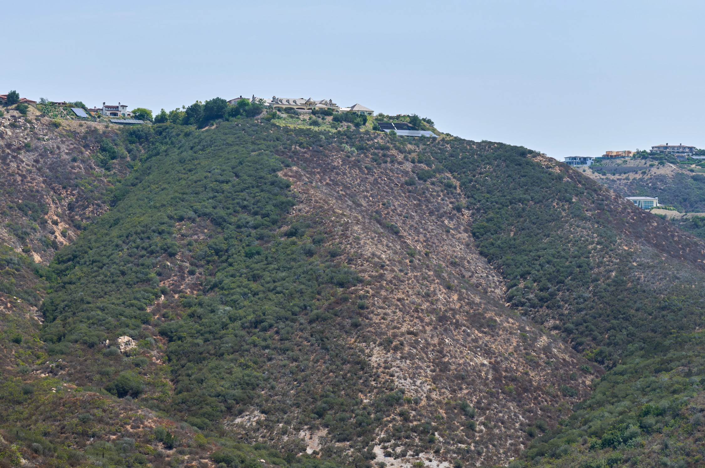 The side of a hill, with brown patches where fires burned vegetation
