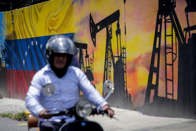 A motorcycle rider passes in front of an oil-themed mural.