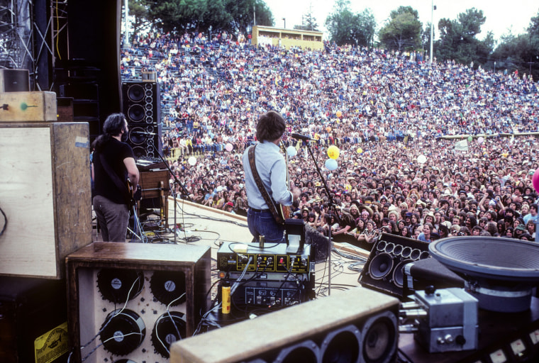 Jerry Garcia, left, and Bob Weir play on stage in front of a large crowd outdoors