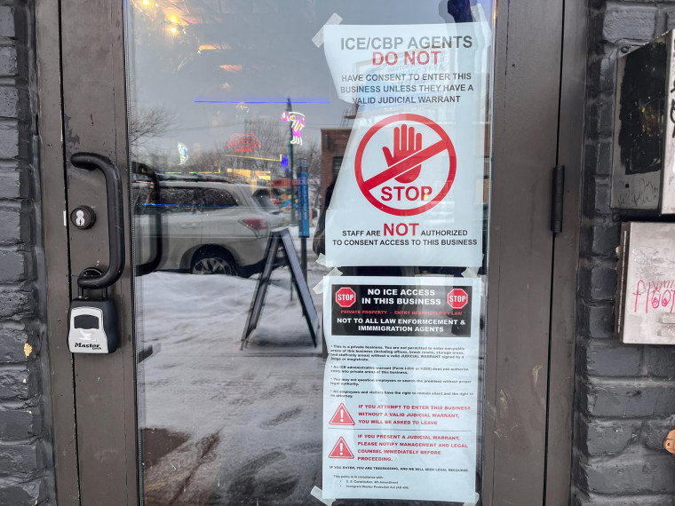 Signs against ICE agents on a storefront door as seen from the outside