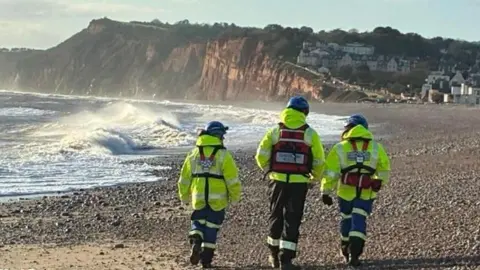 BBC Three people in hi vis on Budleigh Salterton beach.