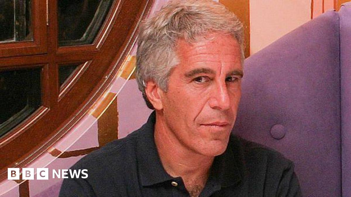 A close photo of Jeffrey Epstein. He sits down and looks at the camera, wearing a dark coloured shirt