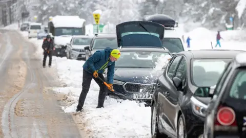 PA Media A man clearing the snow from his car as heavy snow causes disruption on the roads