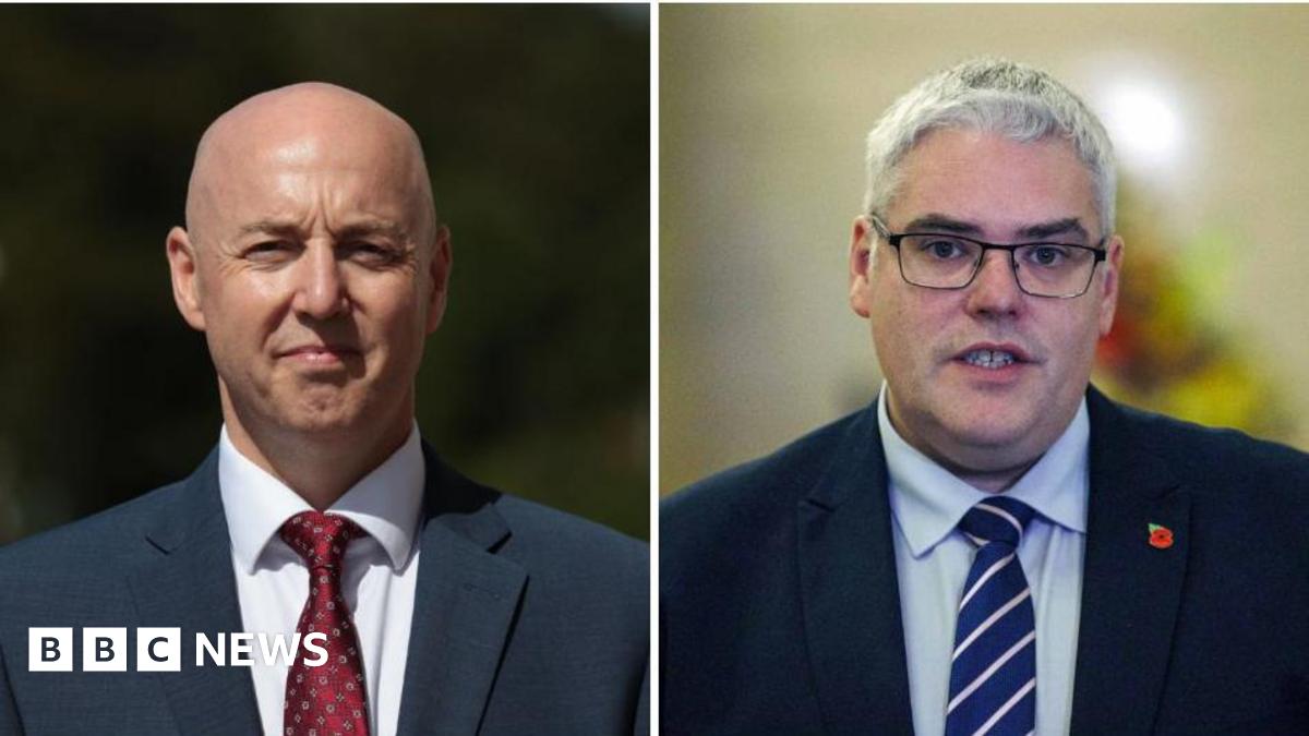 A composite image of Jon Burrows and Gavin Robinson.   Both men are wearing navy suits and are looking ahead towards the camera.  Burrows has a shaven head.  Robinson has short grey hair and black-framed glasses.