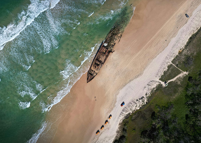 Aerial view of a beach with a shipwreck and footprints, hinting at autopsy results and clues in a teen dingo case.