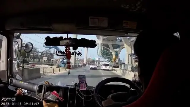 A screenshot from a dashcam video where you can see a crane starting to collapse from an overpass under construction