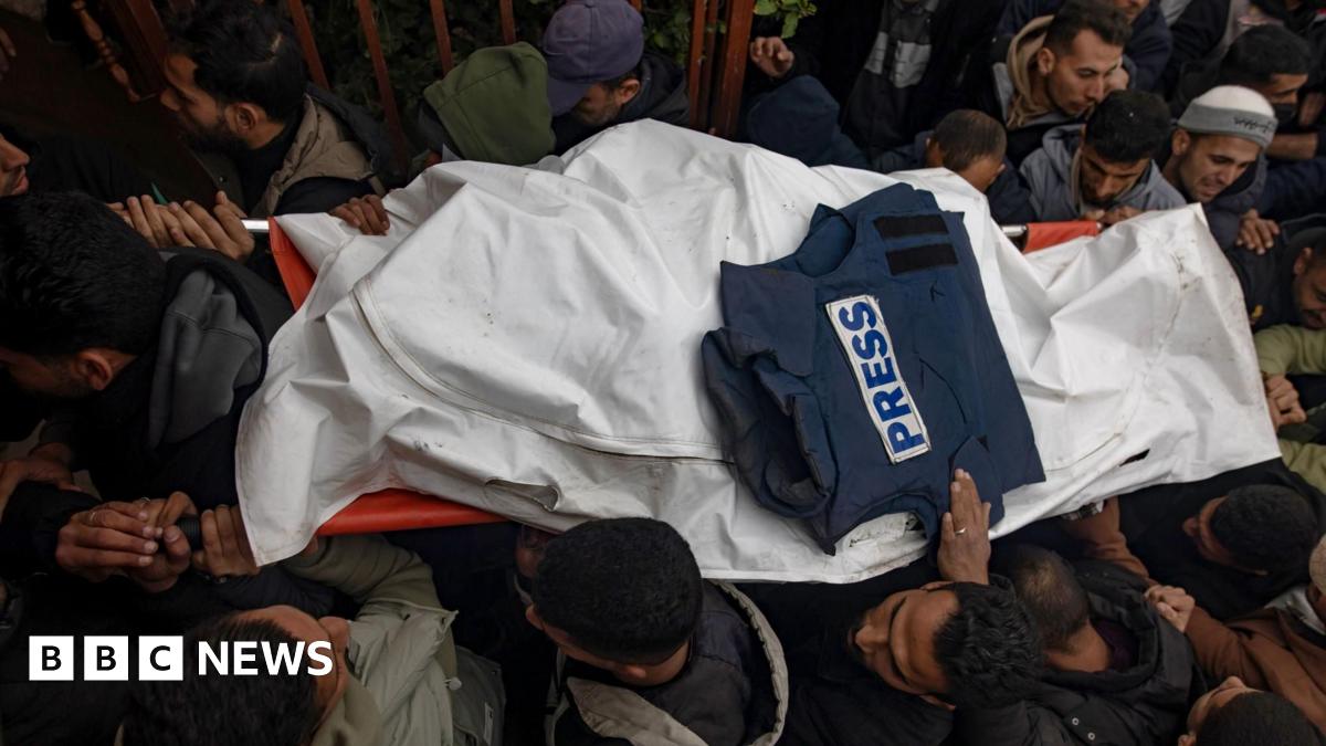 Mourners carry the body of one of the three journalists killed in an Israeli strike, at Nasser hospital in Khan Younis, southern Gaza. The body is carried on a stretcher and covered in a white material with a press jacket laid on top.