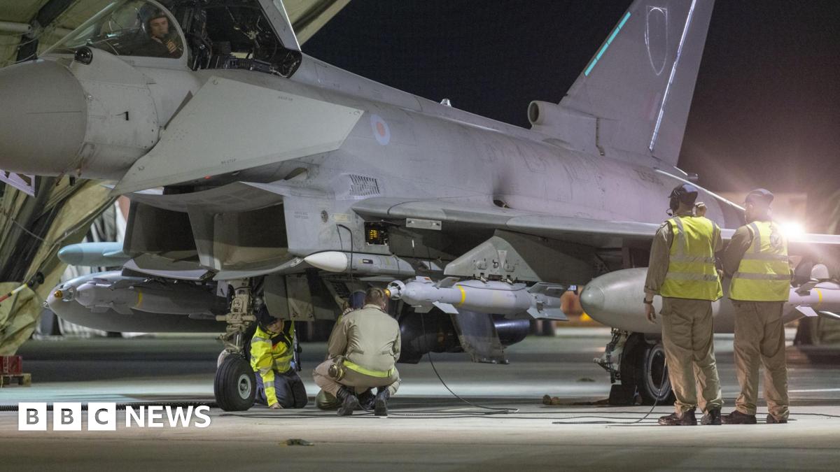 Royal Air Force ground crew preparing an RAF Typhoon fighter jet. It is night-time and the team are working under the floodlights of a hangar.