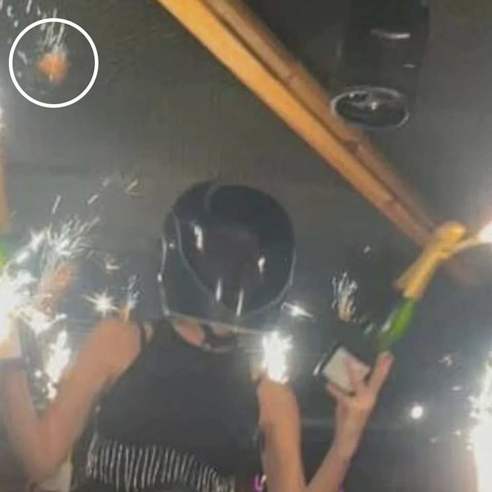 A woman wearing a crash helmet and carrying sparklers appears to set the ceiling of the venue alight