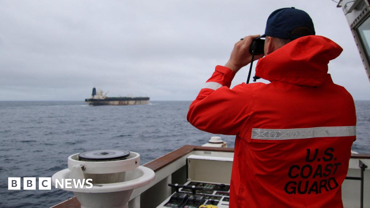 A US Coast Guard official wearing an orange hi-viz jacket looks through binoculars at the Marinera in the Moray Firth