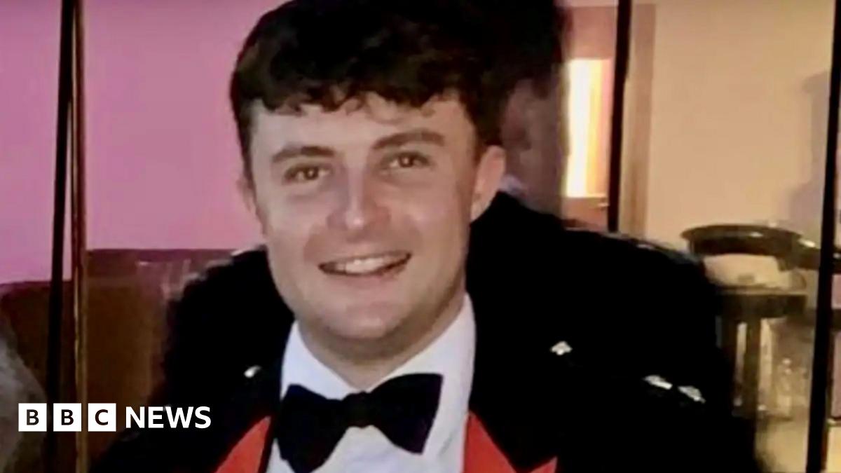 Captain Philip Gilbert Muldowney smiles as he looks into the camera, with short dark hair, wearing a dress suit and bow tie.