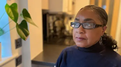 Denise has glasses on and looks out of the window