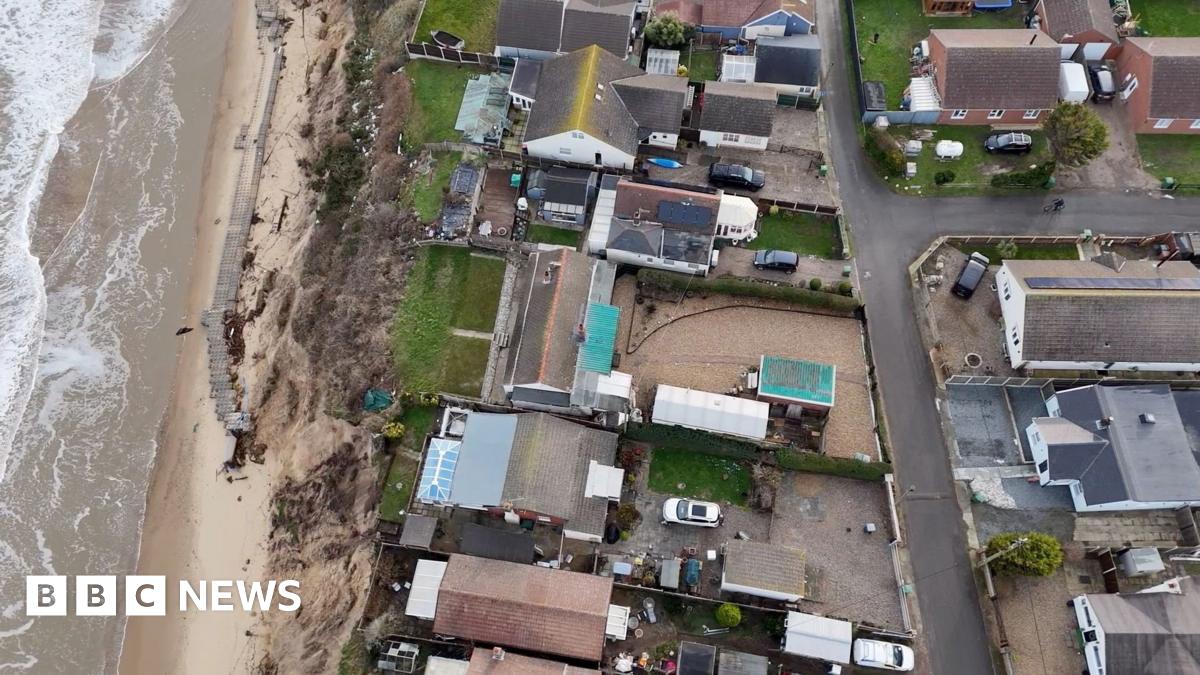 A drone shot above chalets and gardens along a cliff edge.