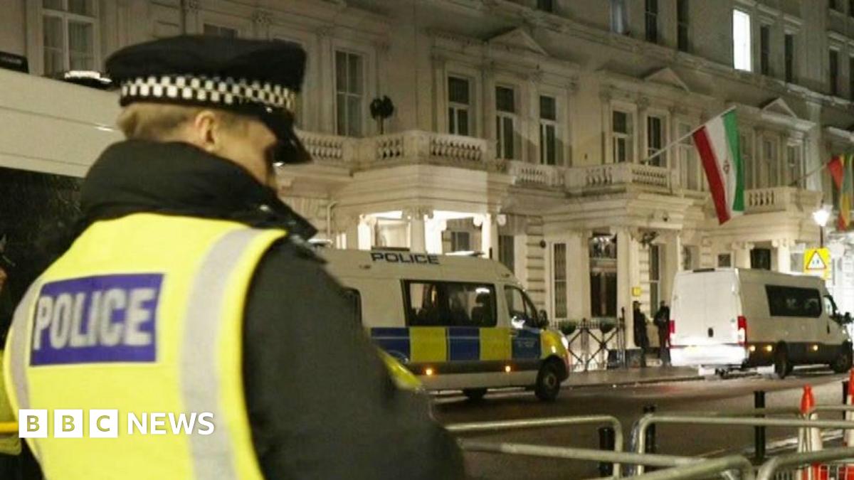 Police officers in hi vis are seen stood around fencing in the street outside the Iranian embassy in London