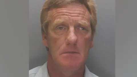 Cheshire Police A police mugshot of Anthony Burns, 63, who has ginger hair and is wearing a light blue collared shirt. He is looking into the camera with a sorrowful expression. 