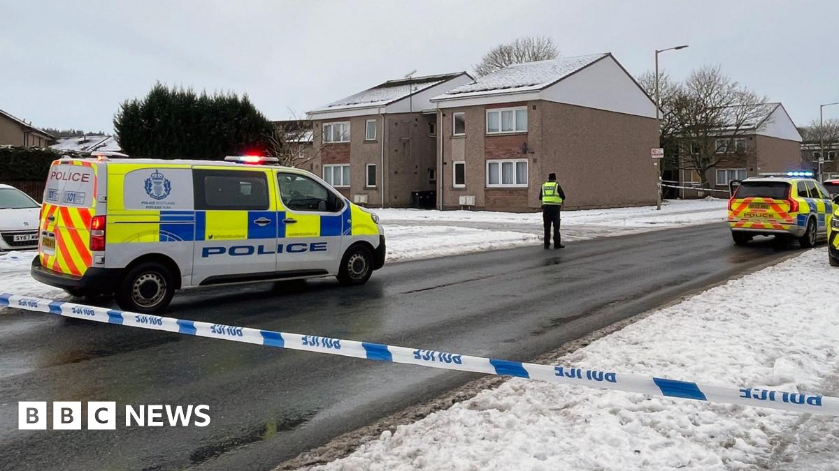 A police van and an officer in a hi-vis vest over black clothing standing next to a snow path in Inverness.