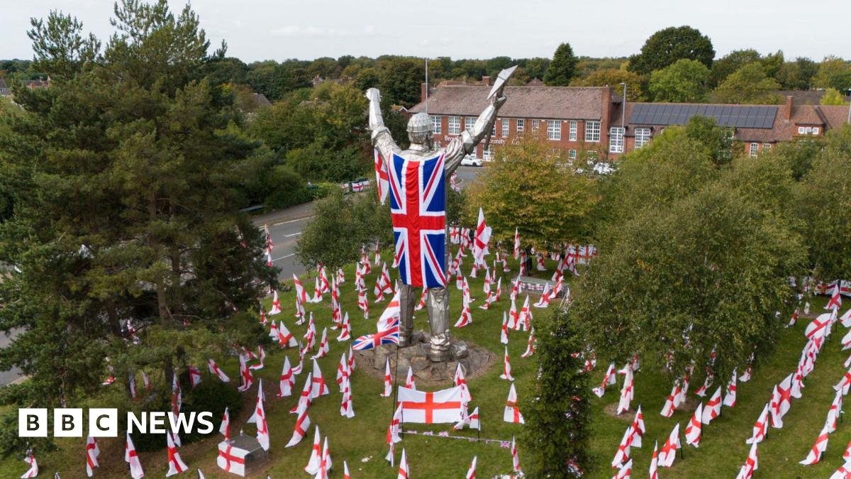A large silver statue of a miner in Brownhills is adorned with a Union Jack Flag worn as a cape with St George's cross flags spread across the ground where the statue stands.
