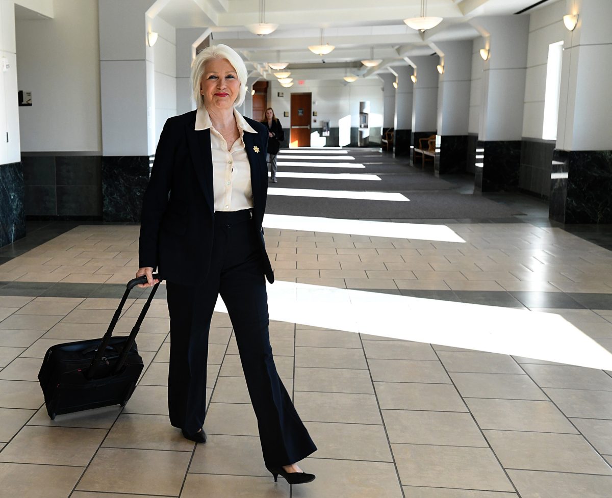 Tina Peters, wearing a dark suit and pulling a wheeled brief case, walks toward the courtroom where she was sentenced for her role in a 2021 breach of her county's election equipment