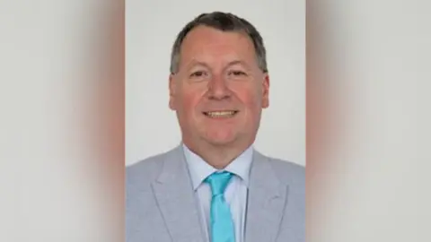 Leicestershire County Council An image of a man in a suit wearing a turquoise tie. 