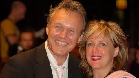 Peter Andrews/Corbis via Getty Images Sarah Fisher, with her blonde hair tousled in a long crop and wearing a pink shawl, with Anthony Head who is wearing a black jacket, white shirt and tie.
The pair have big smiles for photographers.