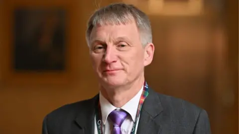 Getty Images Ivan McKee, who has short grey hair, looks at the camera. He is wearing a grey suit and tartan lanyard. 